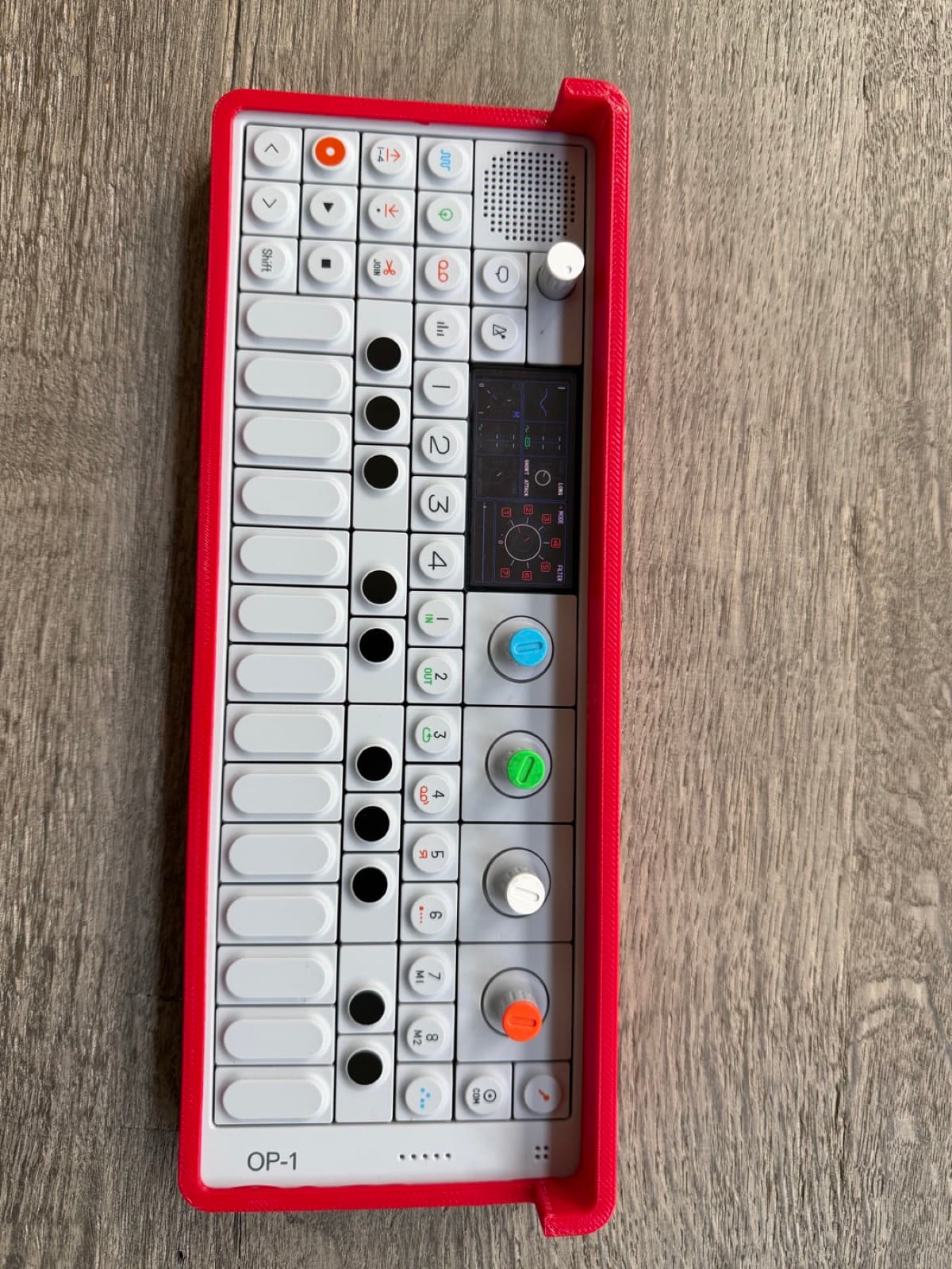 OP-1 in a Signal Red bumper, seen from above, every key and encoder exposed